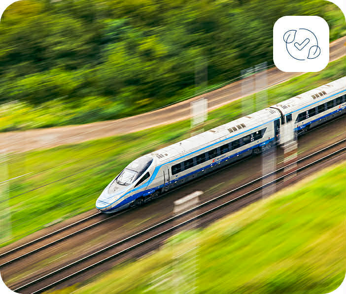 Pociąg dużych prędkości PKP Intercity jedzie przez zielone pola, w rogu ikona liści symbolizująca ekologiczne podróżowanie.