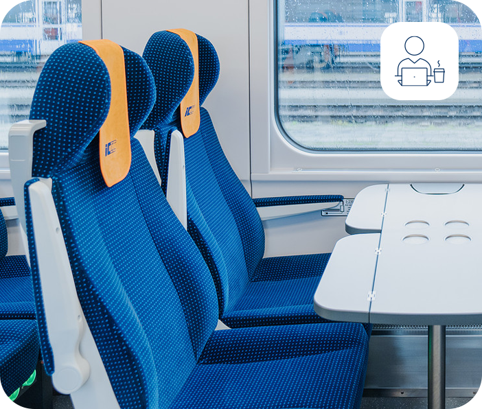 Wnętrze wagonu PKP Intercity – niebieskie fotele przy stoliku z widokiem przez okno i ikoną miejsca do pracy z laptopem.